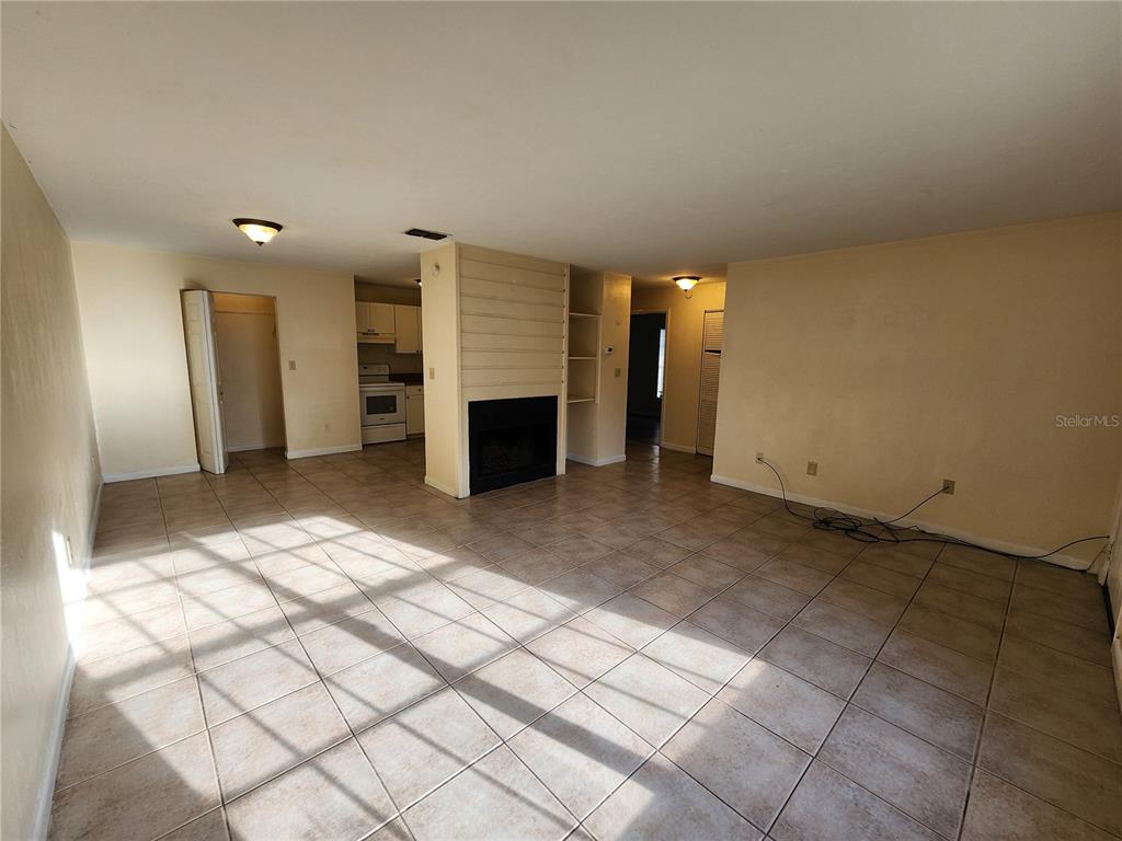 A living room with tile flooring, a central fireplace, and an adjacent kitchen area — 2529 NW 62 PLACE, GAINESVILLE, FL