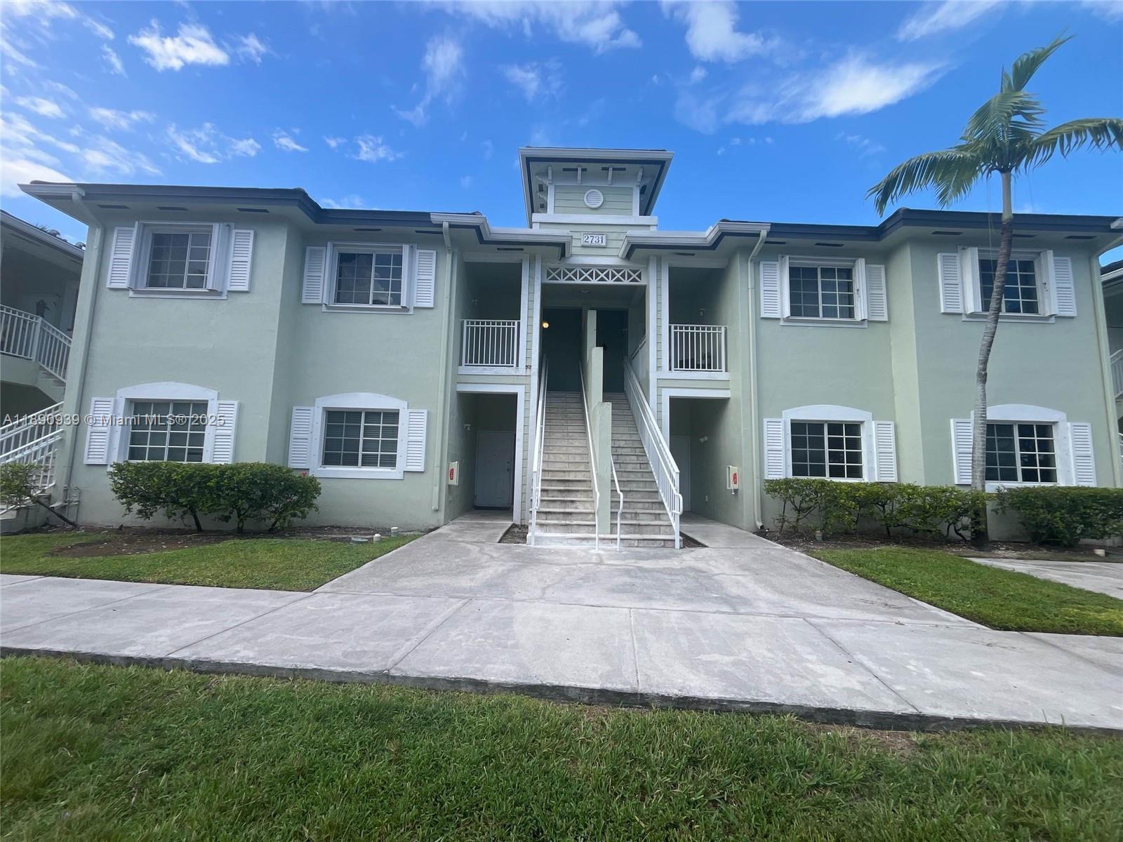 A two-story light green apartment building features a central staircase and white window shutters — 2731 NE 3rd Dr # 203, Homestead FL 33033, HOMESTEAD, FL