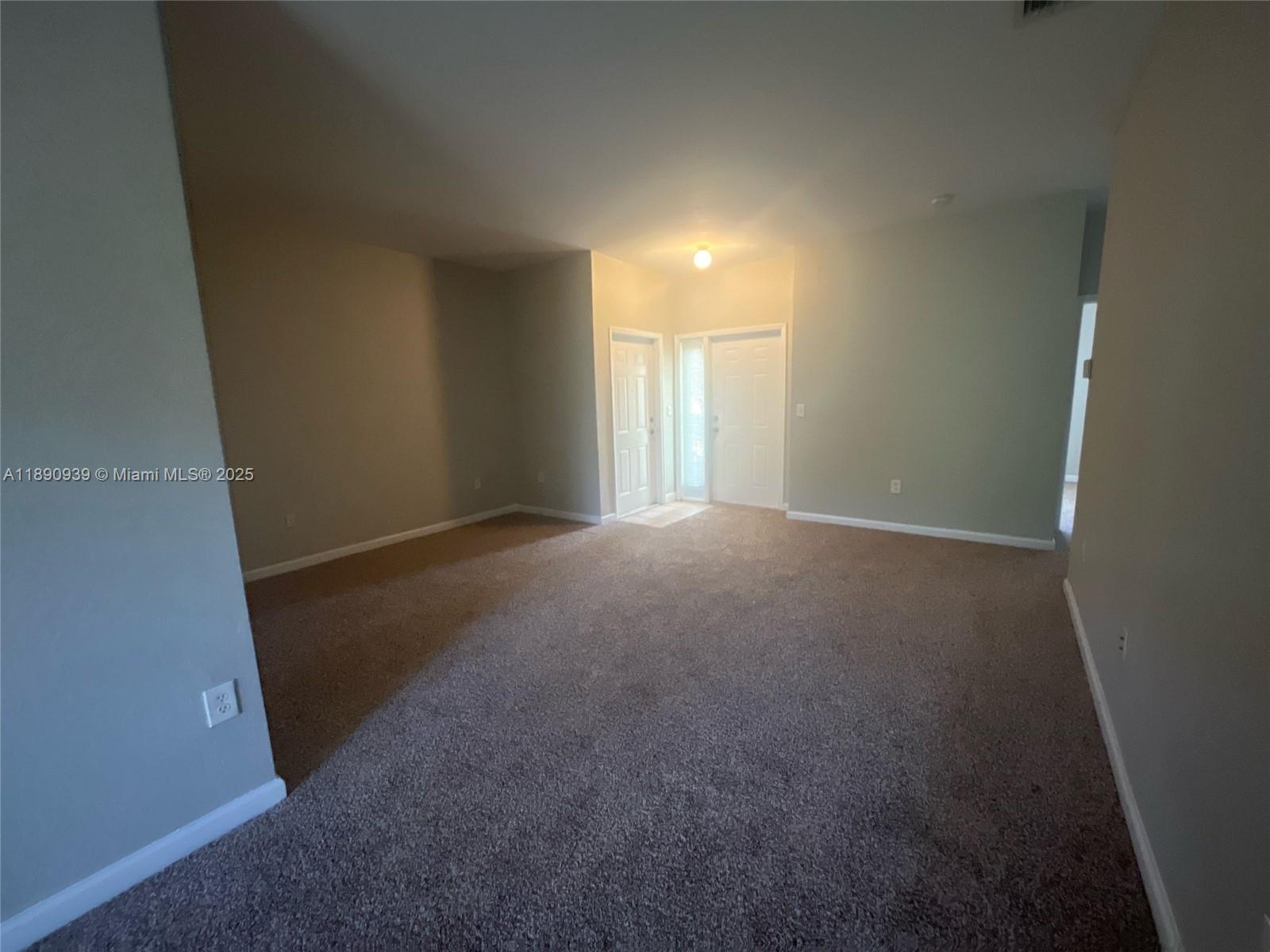 An empty living room features beige carpet, light-colored walls, and a white front door — 2731 NE 3rd Dr # 203, Homestead FL 33033, HOMESTEAD, FL