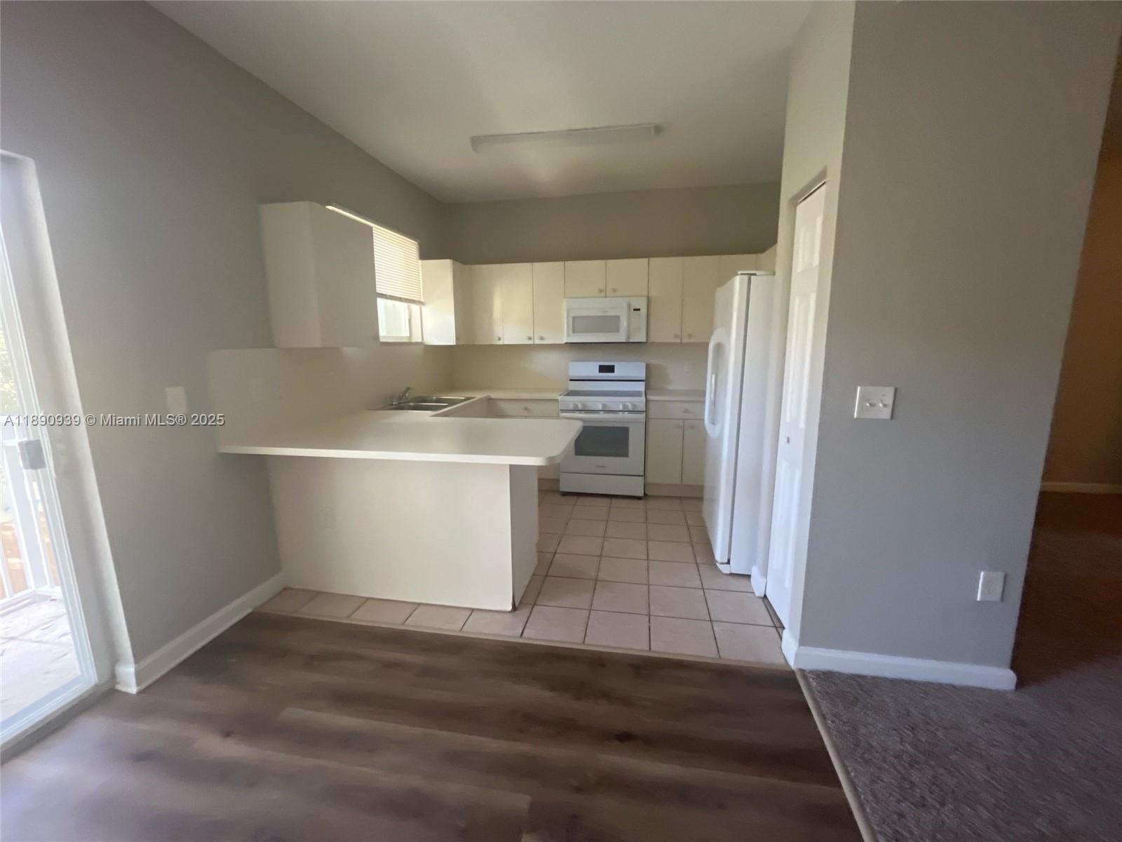 A kitchen features white cabinets, white appliances, a breakfast bar, and tiled flooring — 2731 NE 3rd Dr # 203, Homestead FL 33033, HOMESTEAD, FL