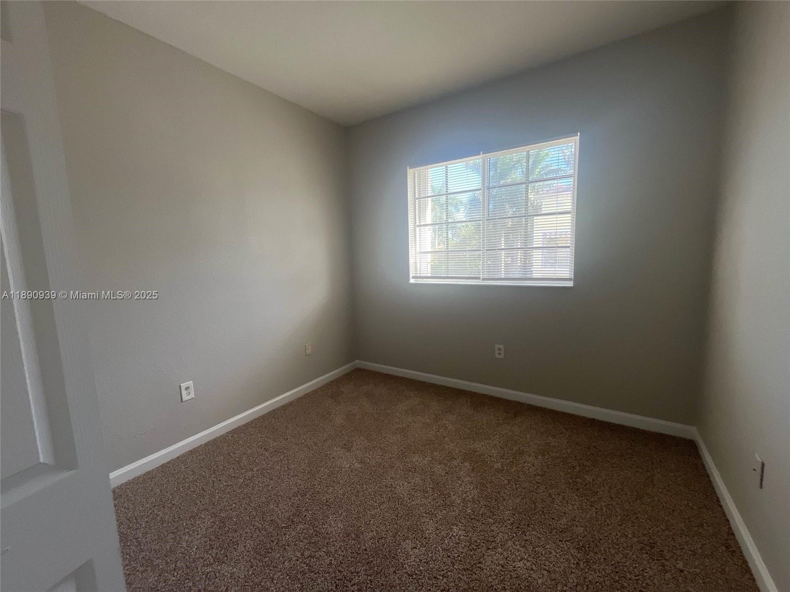 An empty bedroom features gray walls, brown carpet, and a window with white blinds — 2731 NE 3rd Dr # 203, Homestead FL 33033, HOMESTEAD, FL