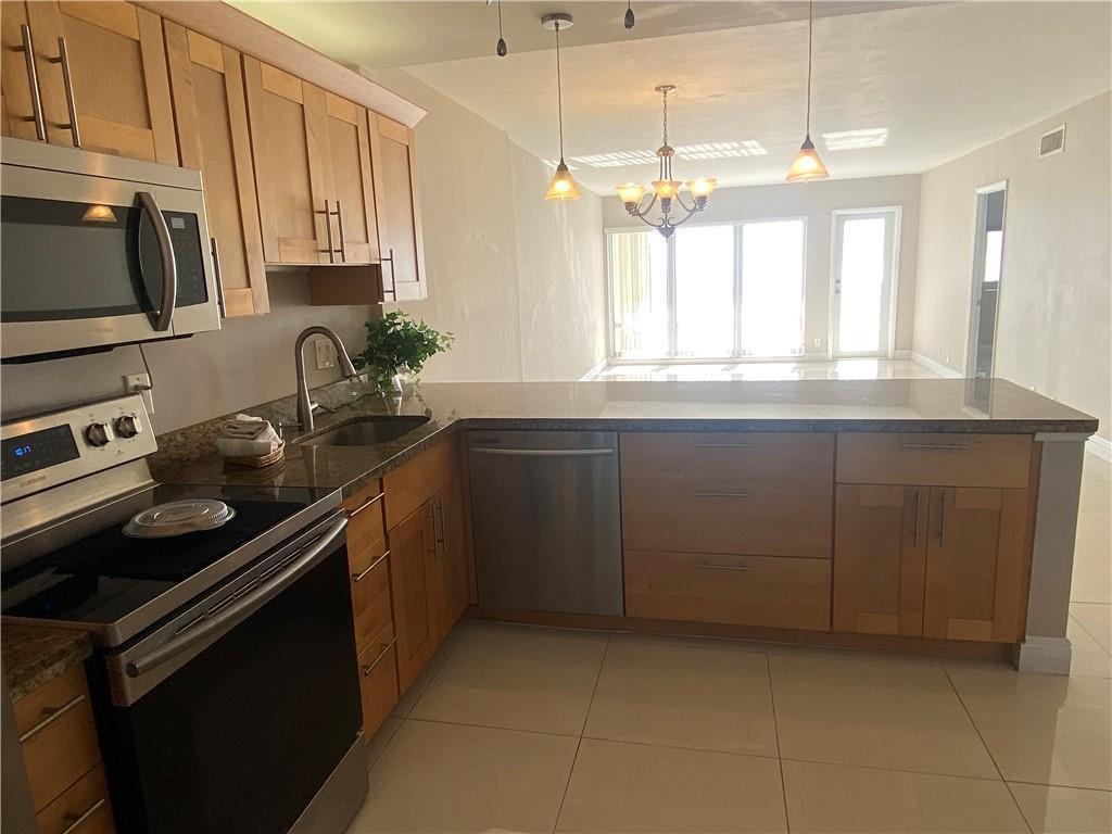 A kitchen features light wood cabinets, granite countertops, stainless steel appliances, and tile flooring — 750 N Ocean Boulevard # 1009, Pompano Beach FL 33062, POMPANO BEACH, FL