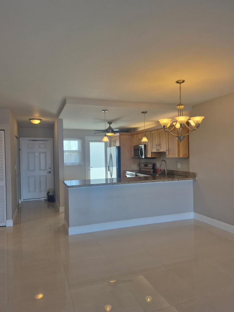 A kitchen with light wood cabinets, granite countertops, and stainless steel appliances overlooks a living area — 750 N Ocean Boulevard # 1009, Pompano Beach FL 33062, POMPANO BEACH, FL