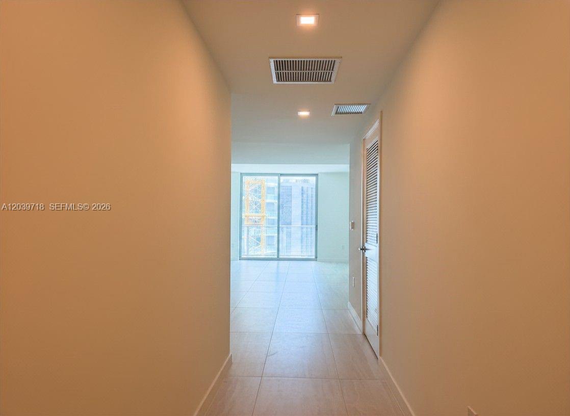A hallway with light-colored tile flooring leads to a room with floor-to-ceiling windows — 77 SE 5th St # 1903, Miami FL 33131, MIAMI, FL