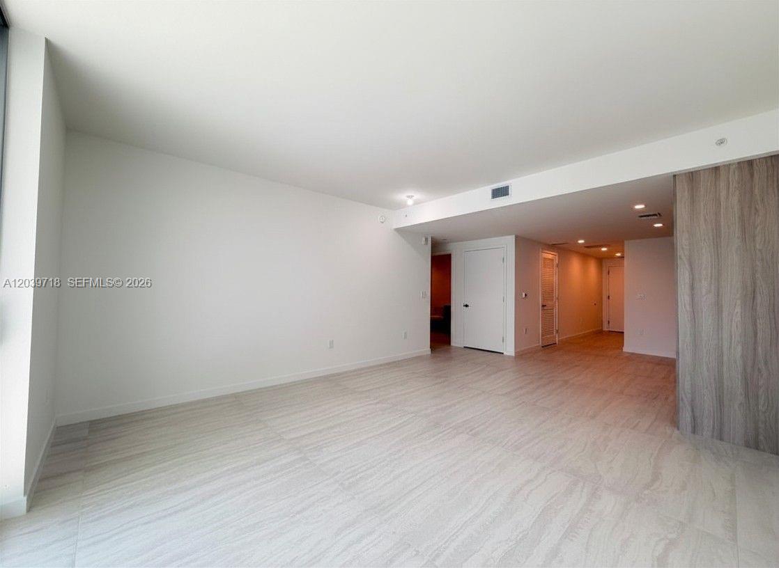 An empty room features light-colored wood-look tile flooring, white walls, and a wood-paneled accent wall — 77 SE 5th St # 1903, Miami FL 33131, MIAMI, FL
