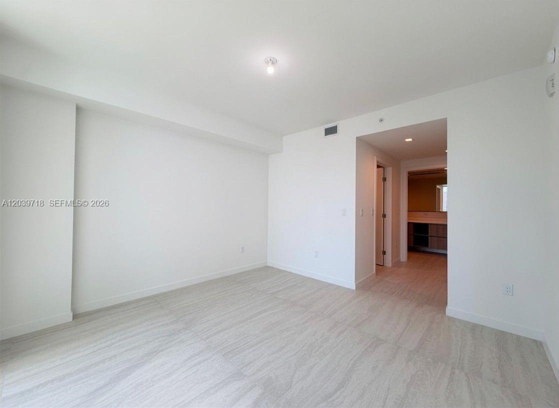 An empty room features light-colored wood-look flooring, white walls, and a doorway leading inside — 77 SE 5th St # 1903, Miami FL 33131, MIAMI, FL