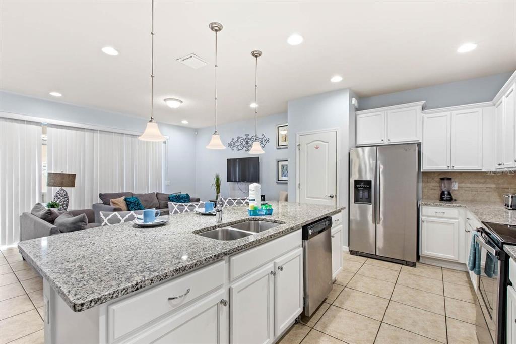 A kitchen with a granite island and stainless steel appliances opens into a living area — 2015 MAJORCA DRIVE, KISSIMMEE, FL
