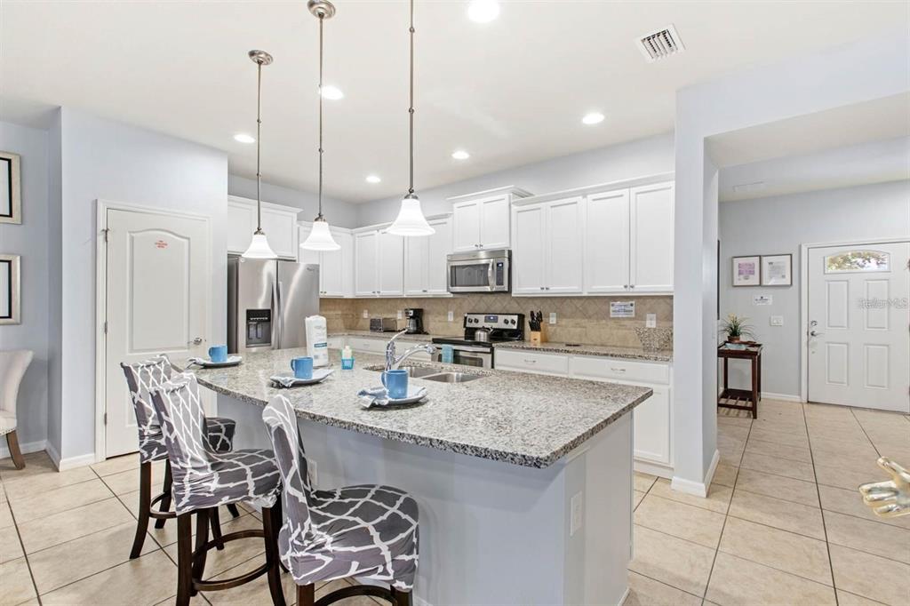 A kitchen features white cabinets, granite countertops, a central island with seating, and tile flooring — 2015 MAJORCA DRIVE, KISSIMMEE, FL