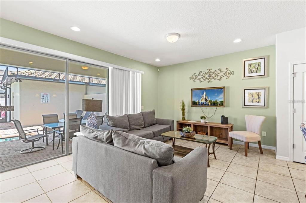 A living room with tile floors, gray sofas, a television, and a sliding glass door — 2015 MAJORCA DRIVE, KISSIMMEE, FL