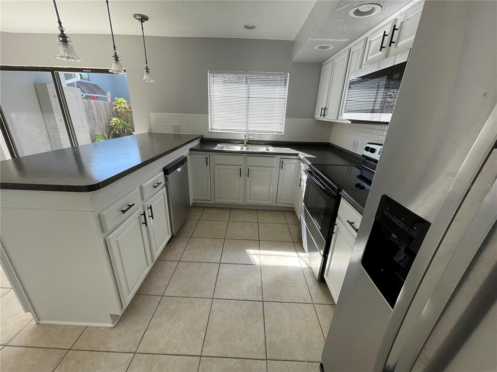 A kitchen with white cabinets, dark countertops, tile flooring, and a stainless steel refrigerator — 3307 KILMER DRIVE UNIT 3307, LAKELAND, FL