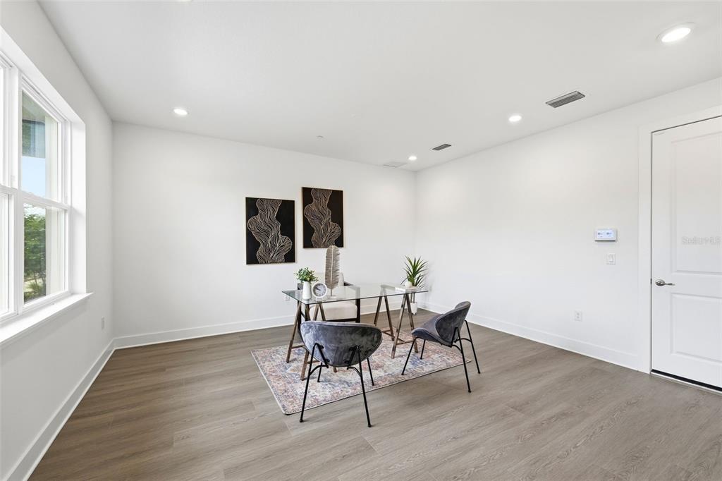 A bright home office features wood-look flooring, white walls, a glass desk, and two chairs — 9156 SINATRA LANE, ORLANDO, FL