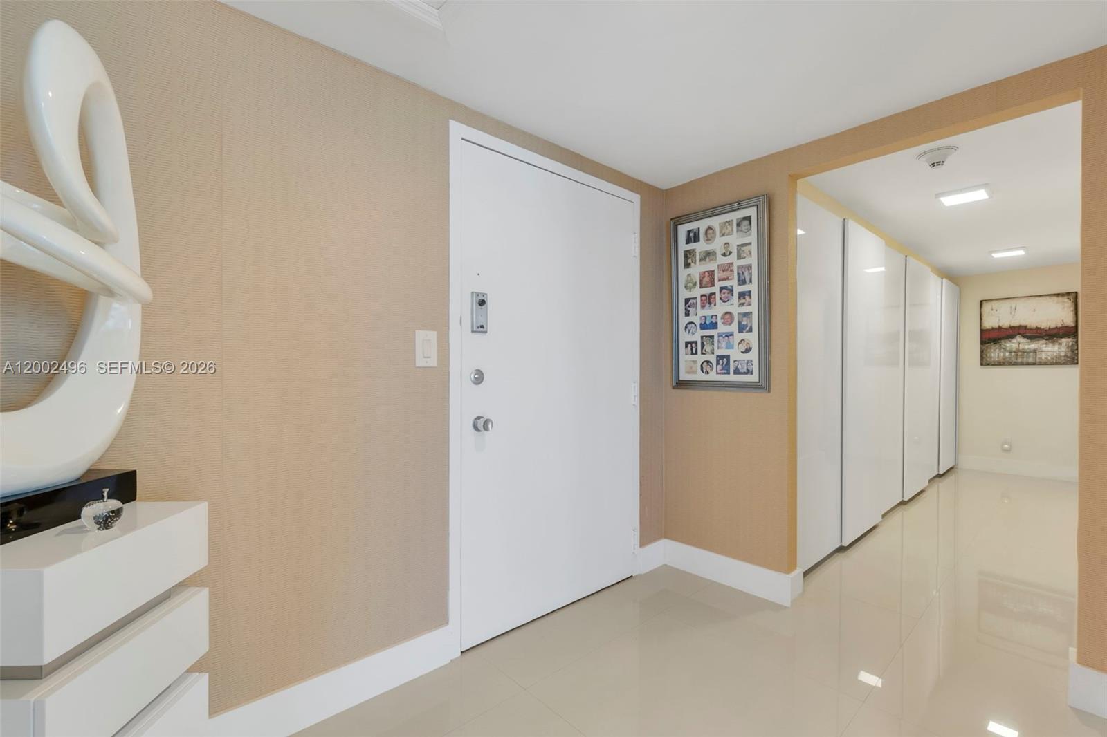 An entryway features a white door, beige textured wallpaper, and a hallway with closets — 5660 Collins Ave # 4B, Miami Beach FL 33140, MIAMI BEACH, FL