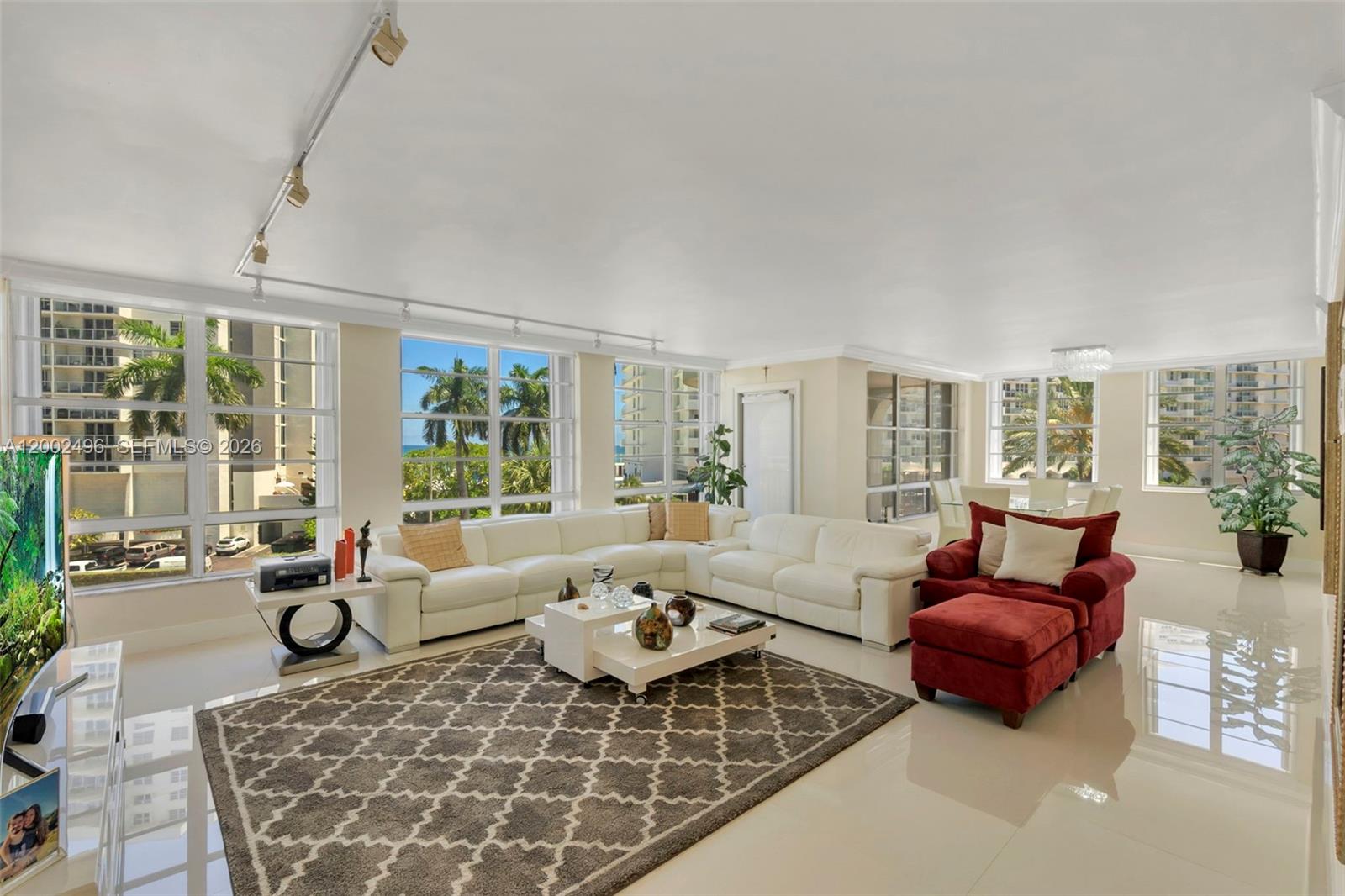 A bright living room features white tile floors, a large sectional sofa, and floor-to-ceiling windows — 5660 Collins Ave # 4B, Miami Beach FL 33140, MIAMI BEACH, FL