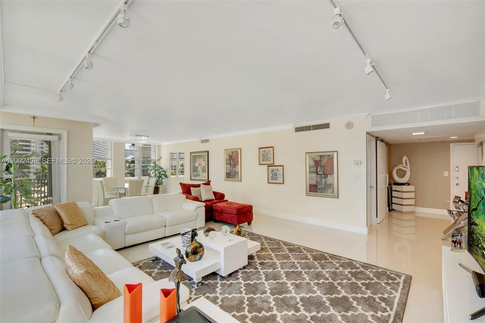 A bright living room features white leather sofas, a red chaise, and a patterned rug — 5660 Collins Ave # 4B, Miami Beach FL 33140, MIAMI BEACH, FL