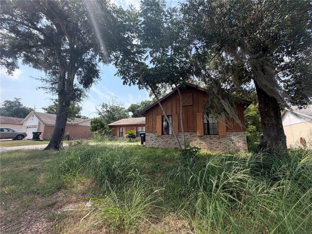 A single-story house with wood siding and brick accents sits behind overgrown grass and trees — 6234 SPARLING HILLS CIRCLE, ORLANDO, FL