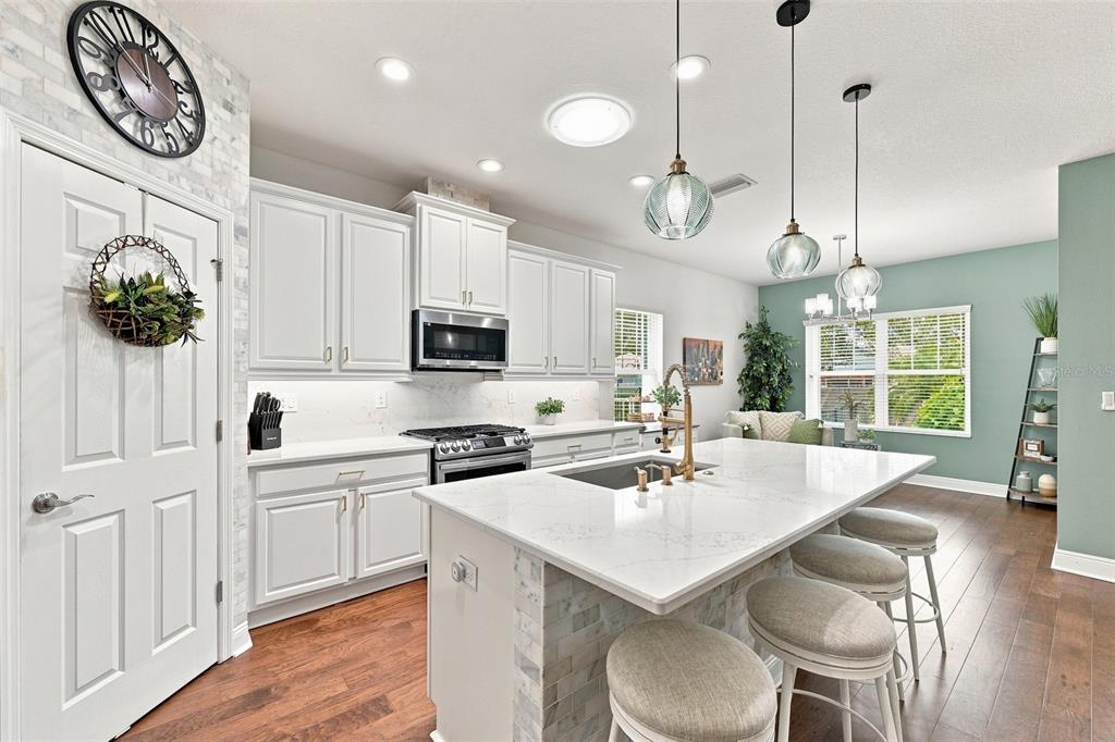 A modern kitchen features white cabinetry, a large quartz island with seating, and wood flooring — 6517 NESTALL COURT, APOLLO BEACH, FL