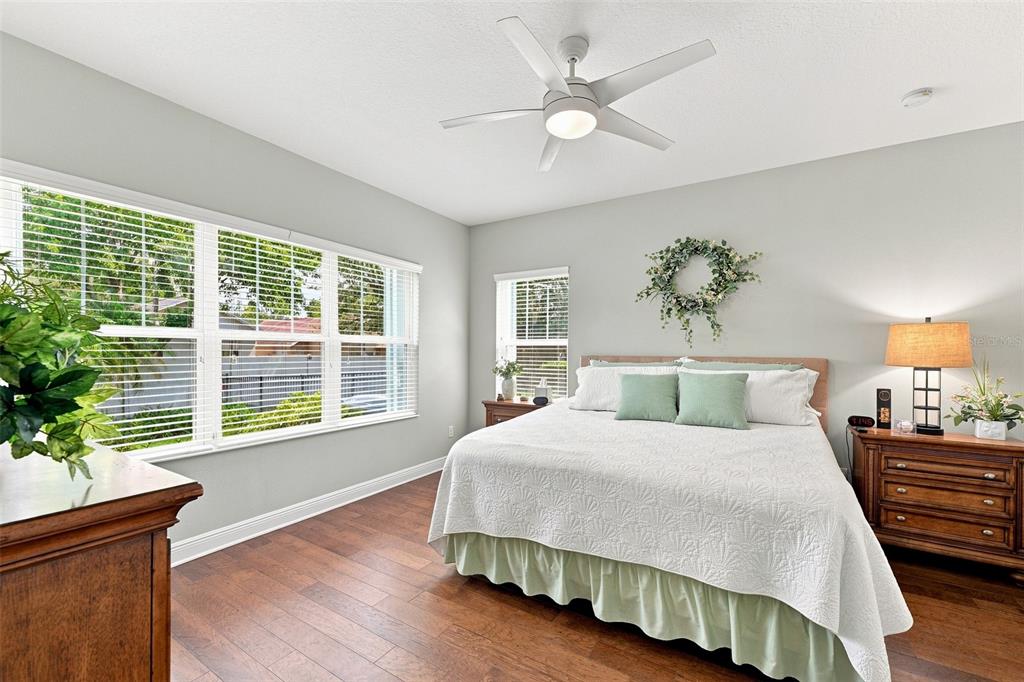 A bedroom features a king bed, wood flooring, a ceiling fan, and large windows — 6517 NESTALL COURT, APOLLO BEACH, FL
