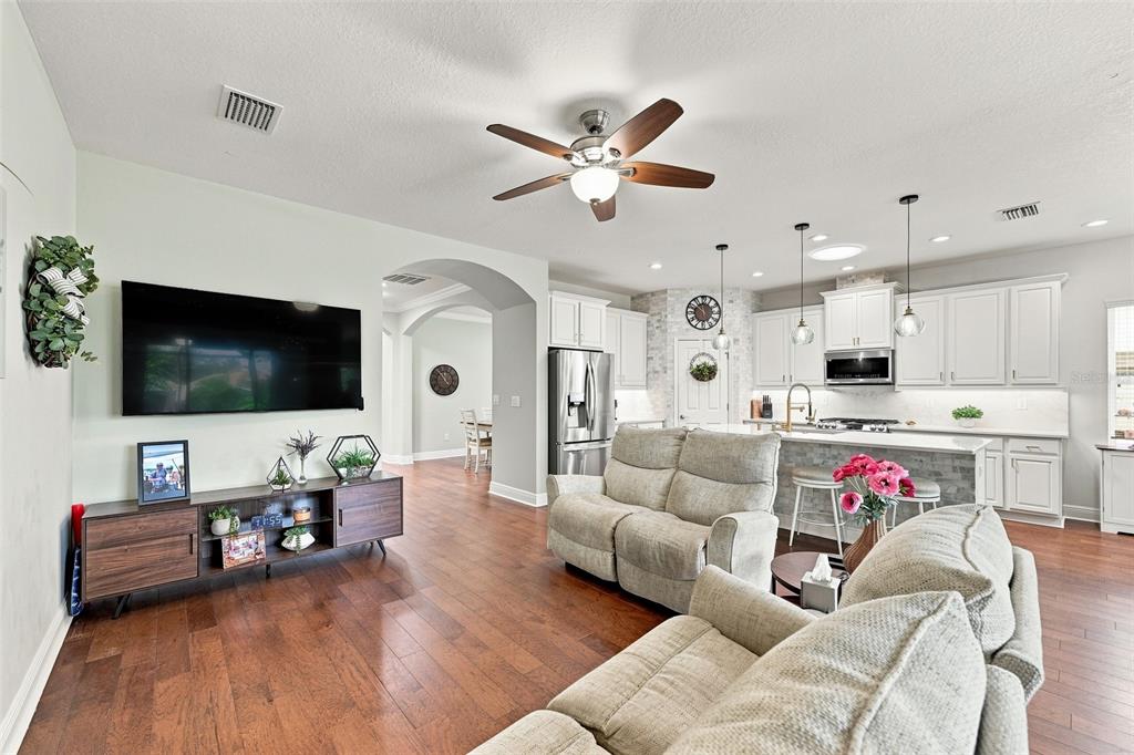 An open-concept living room and kitchen featuring hardwood floors, a ceiling fan, and white cabinetry — 6517 NESTALL COURT, APOLLO BEACH, FL