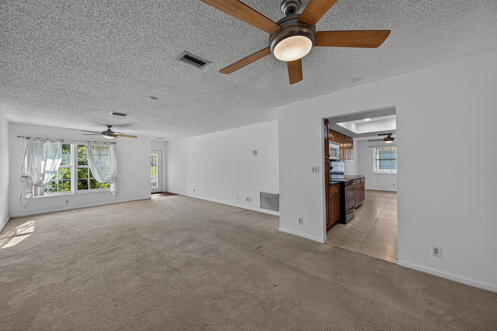A carpeted living room with a ceiling fan opens into a tiled kitchen area — 4234 NW 3rd Way, Boca Raton FL 33431, BOCA RATON, FL
