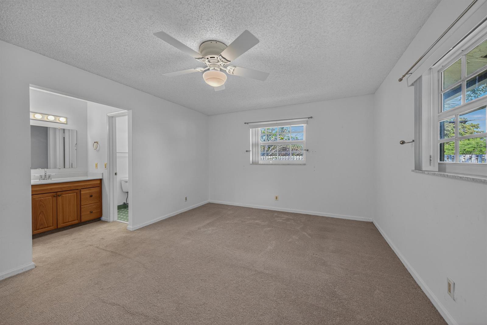 A bedroom with beige carpet, white walls, a ceiling fan, and an attached bathroom — 4234 NW 3rd Way, Boca Raton FL 33431, BOCA RATON, FL