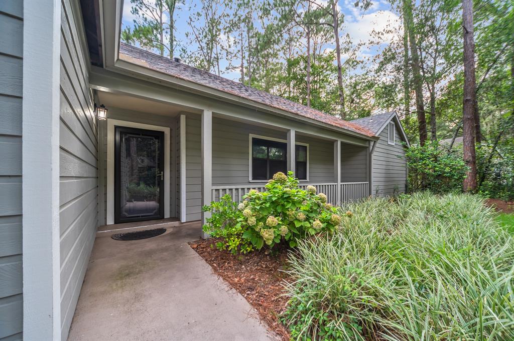 A covered porch leads to the front door of a gray house with wood siding — 8025 SW 47TH COURT, GAINESVILLE, FL