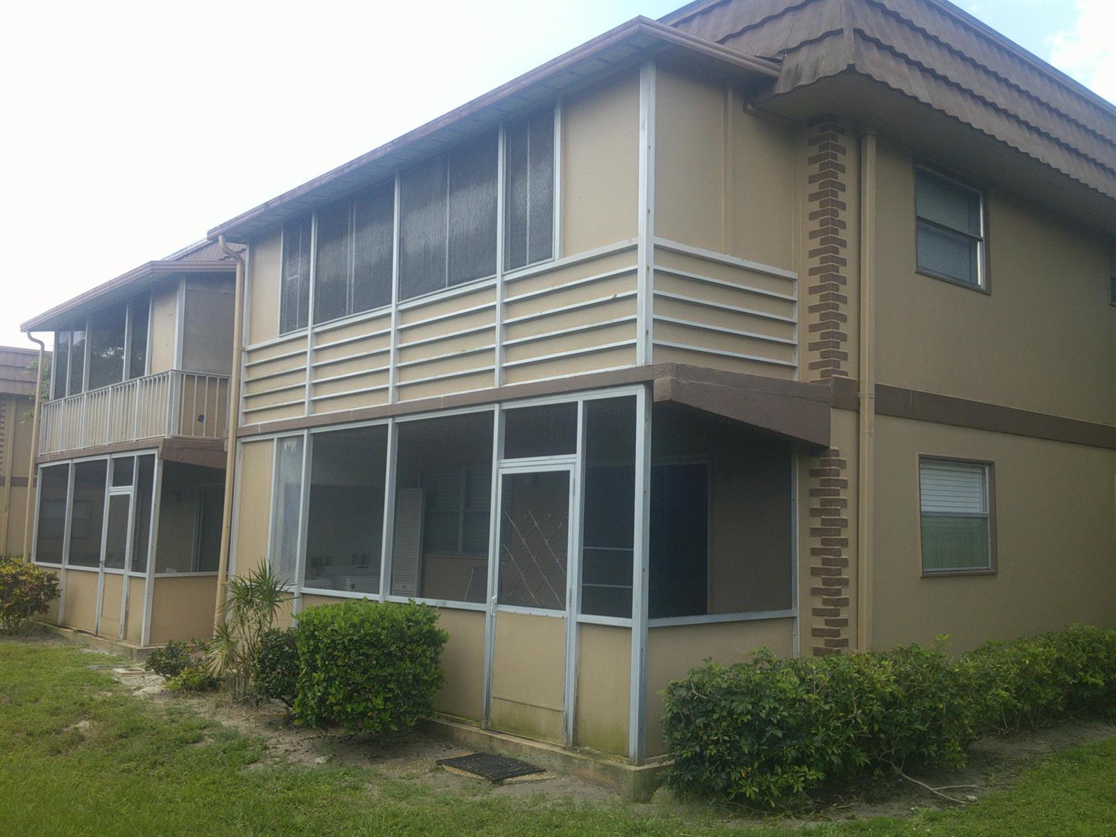 Exterior view of a two-story apartment building with screened-in porches and tan siding — 588 Brittany M, Delray Beach FL 33446, DELRAY BEACH, FL