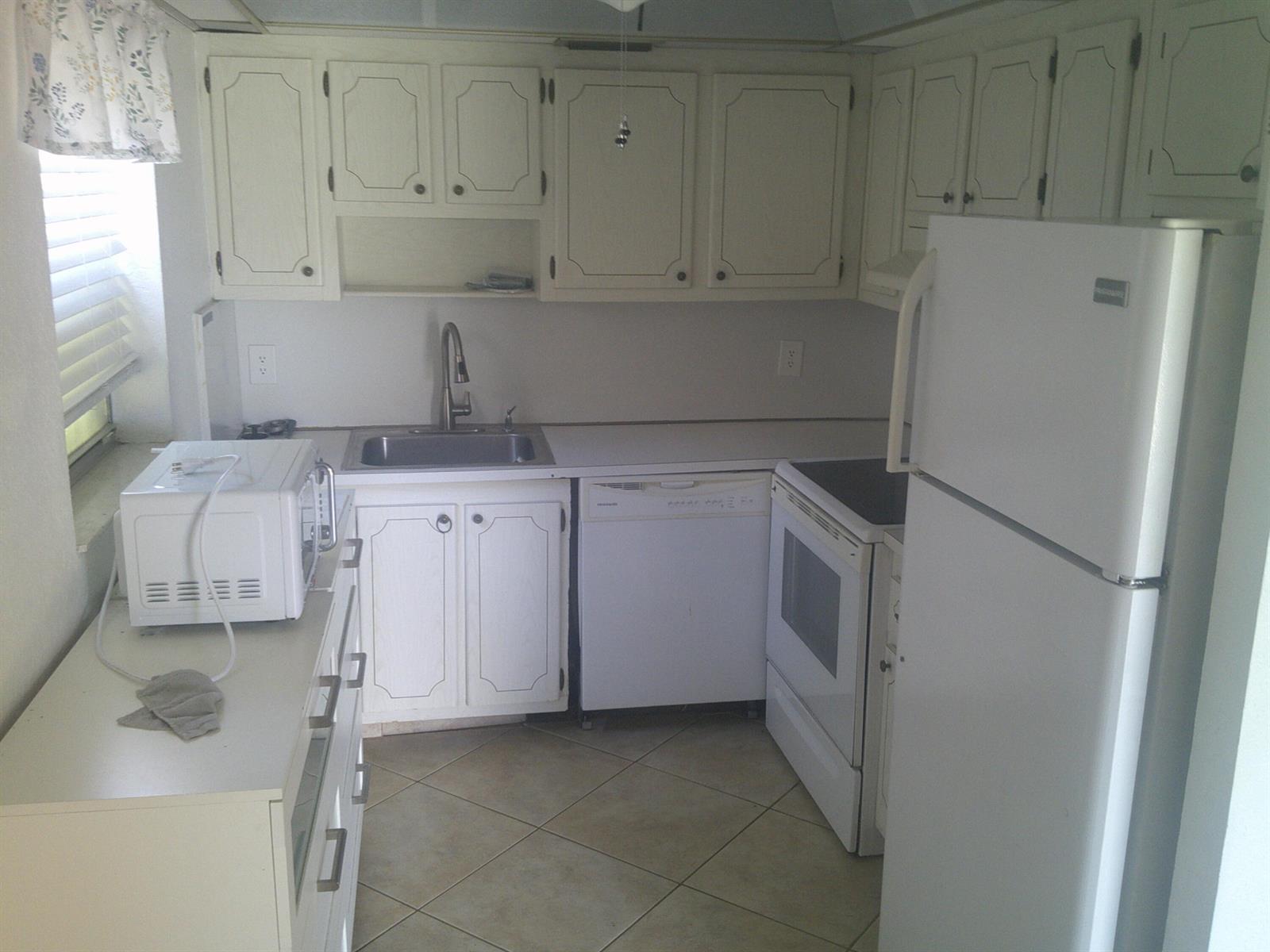 A small kitchen features white cabinets, white appliances, a stainless steel sink, and tile flooring — 588 Brittany M, Delray Beach FL 33446, DELRAY BEACH, FL