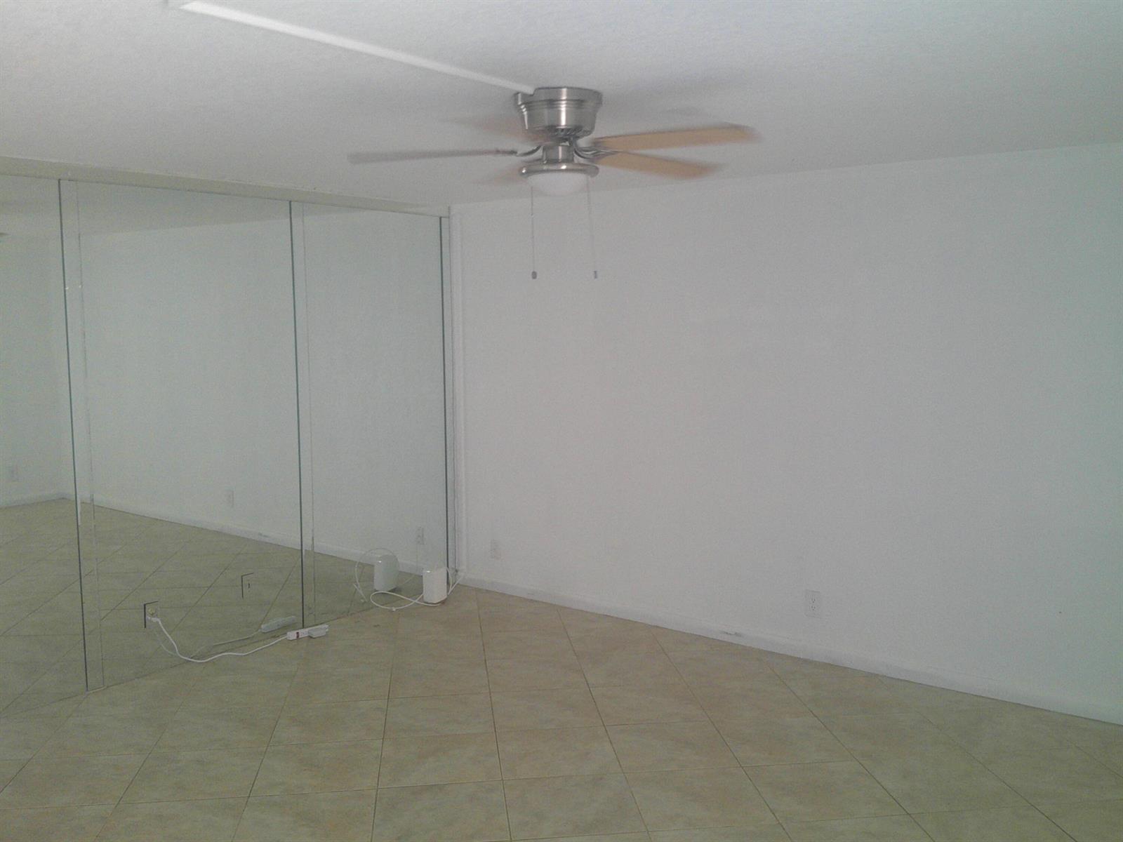 An empty room with beige tile flooring, white walls, a ceiling fan, and mirrored closet doors — 588 Brittany M, Delray Beach FL 33446, DELRAY BEACH, FL