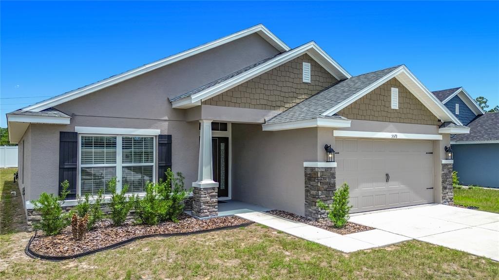 A single-story house features a tan stucco exterior, stone accents, and a two-car garage — 5578 CORAL REEF COURT, SPRING HILL, FL
