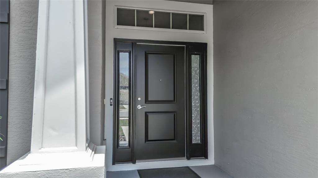 A dark front door with side lights and a transom window sits under a porch — 5578 CORAL REEF COURT, SPRING HILL, FL