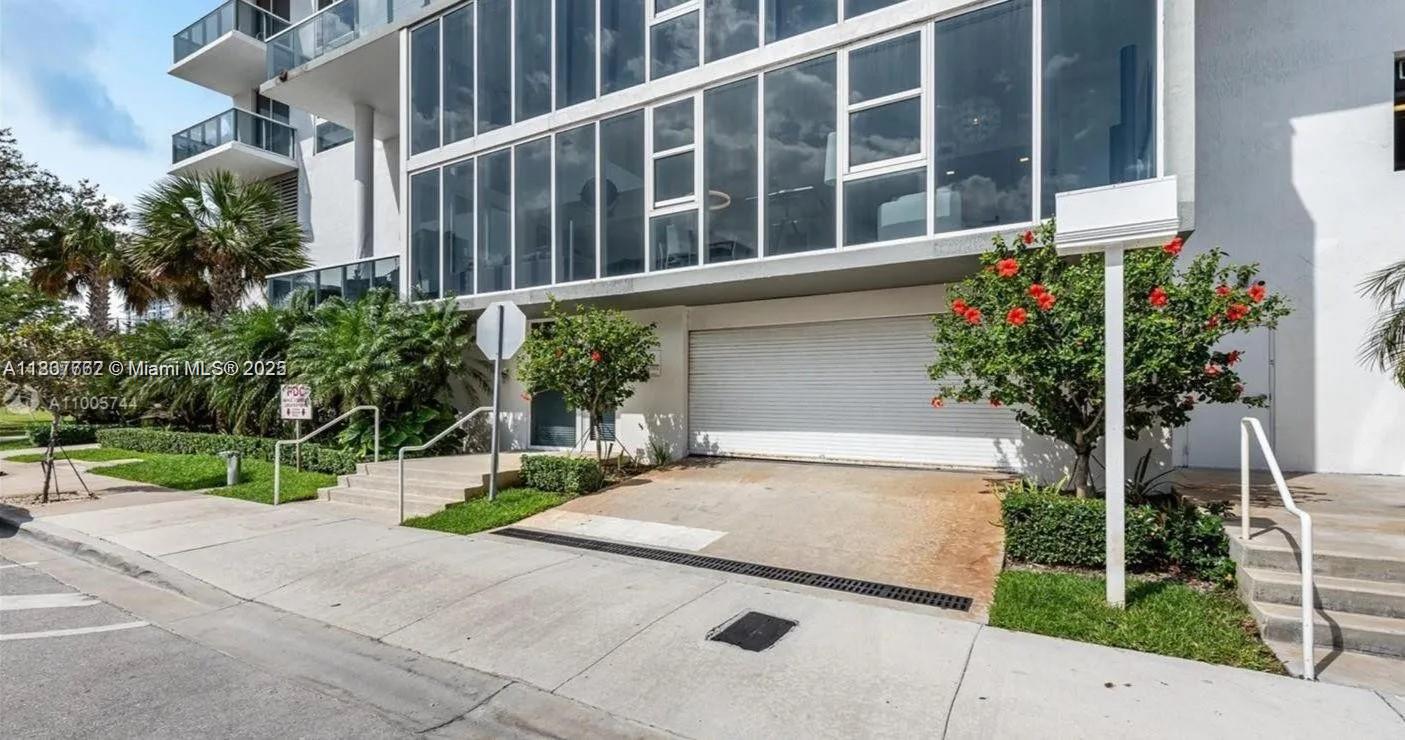 The exterior of a modern multi-story building features a white roll-up garage door and landscaping — 600 NE 27th St # 105, Miami FL 33137, MIAMI, FL