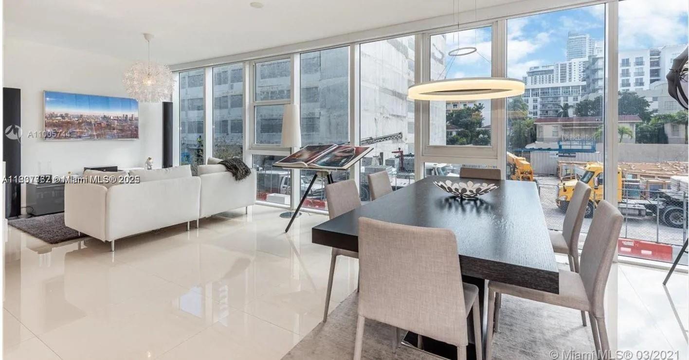 A modern dining and living area features floor-to-ceiling windows overlooking a nearby construction site — 600 NE 27th St # 105, Miami FL 33137, MIAMI, FL