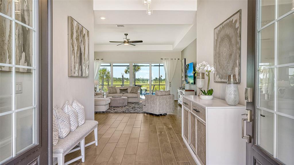 A bright entryway leads into a living room with wood-look tile floors and glass doors — 12453 WELLEN GOLF STREET, VENICE, FL