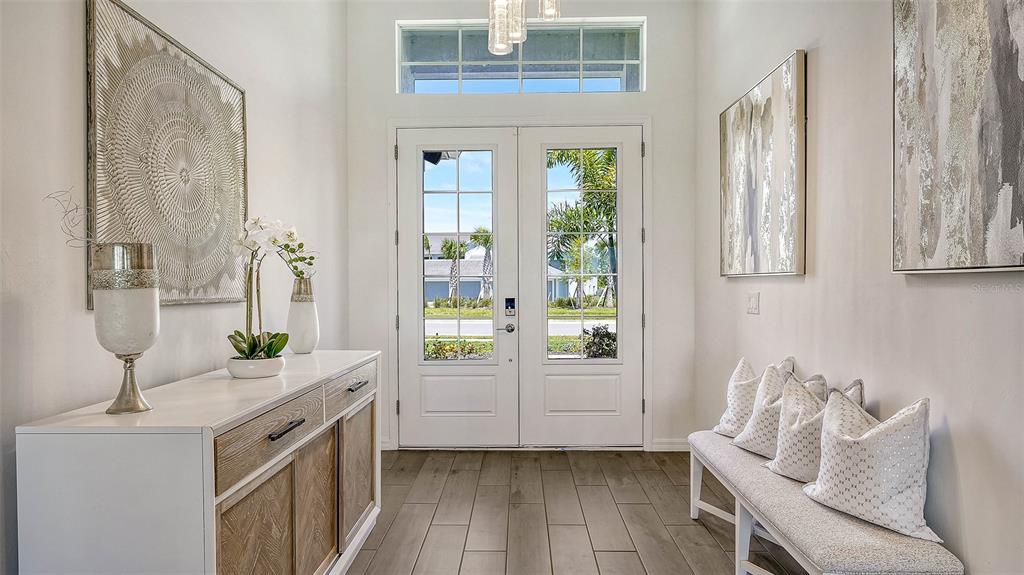 A bright entryway features a white console table, a bench with pillows, and double glass doors — 12453 WELLEN GOLF STREET, VENICE, FL