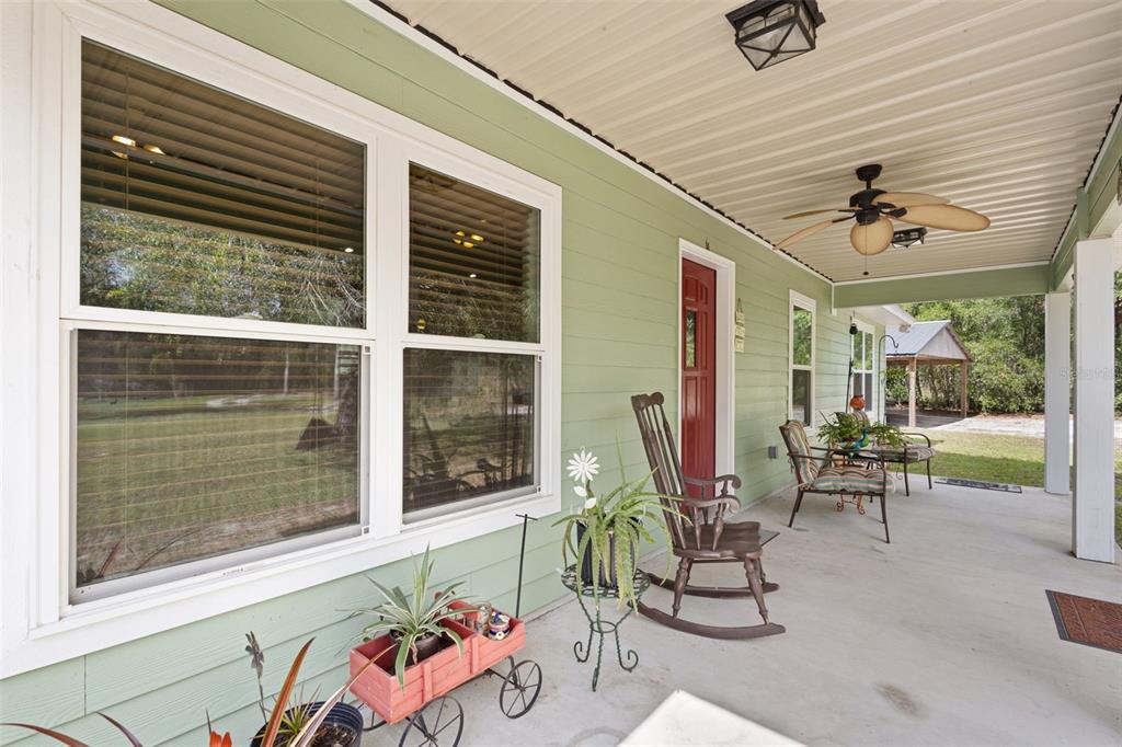 A covered porch features light green siding, a red front door, and outdoor seating — 10250 NE 5TH AVENUE, BRANFORD, FL