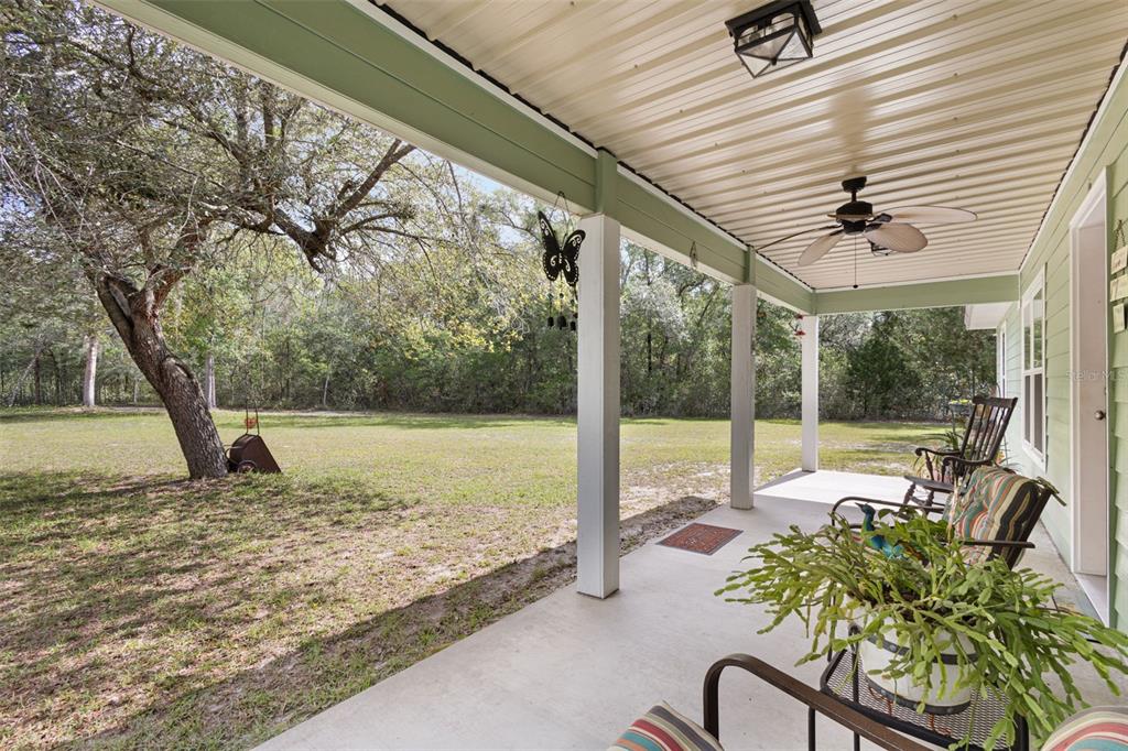A covered porch with a ceiling fan overlooks a grassy yard and wooded area — 10250 NE 5TH AVENUE, BRANFORD, FL
