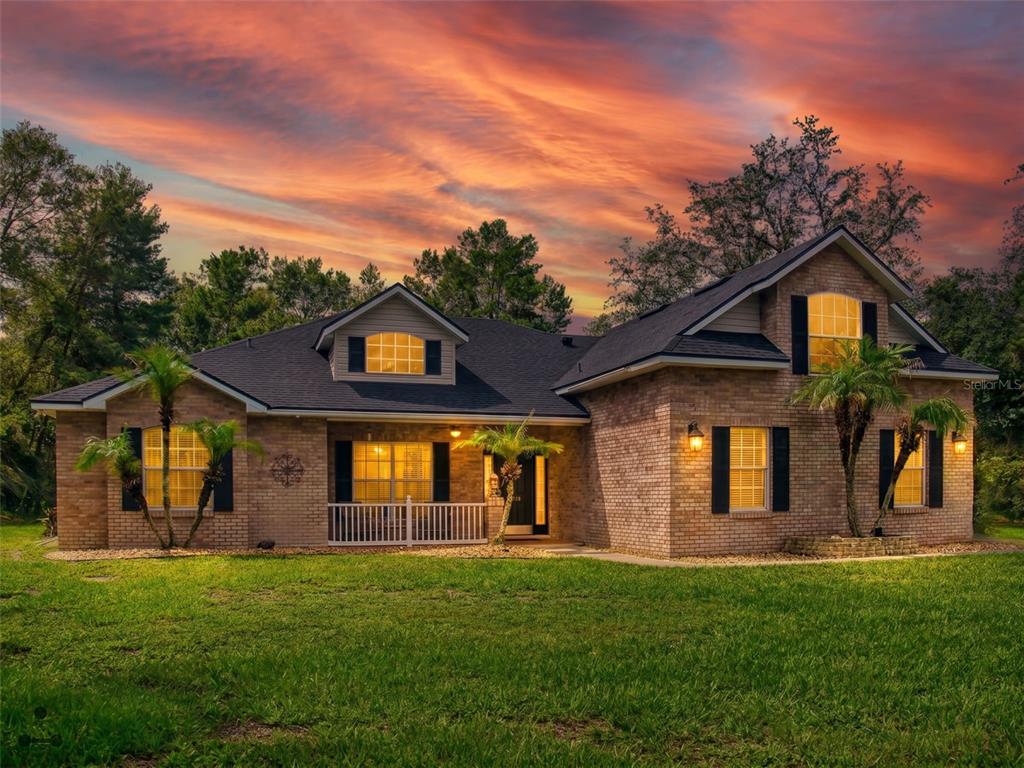 A two-story brick house with a dark shingled roof stands under a sunset sky — 3040 BUTLER RIDGE ROAD, DELTONA, FL