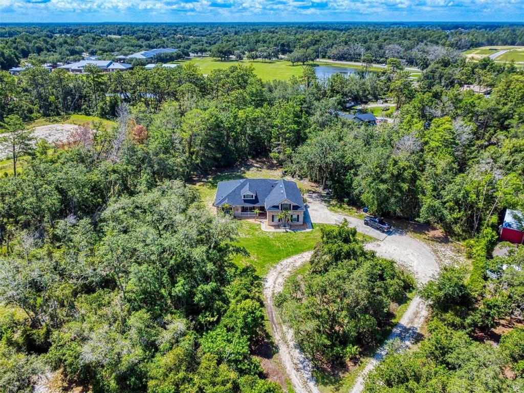 An aerial view shows a house surrounded by dense trees and a gravel driveway — 3040 BUTLER RIDGE ROAD, DELTONA, FL