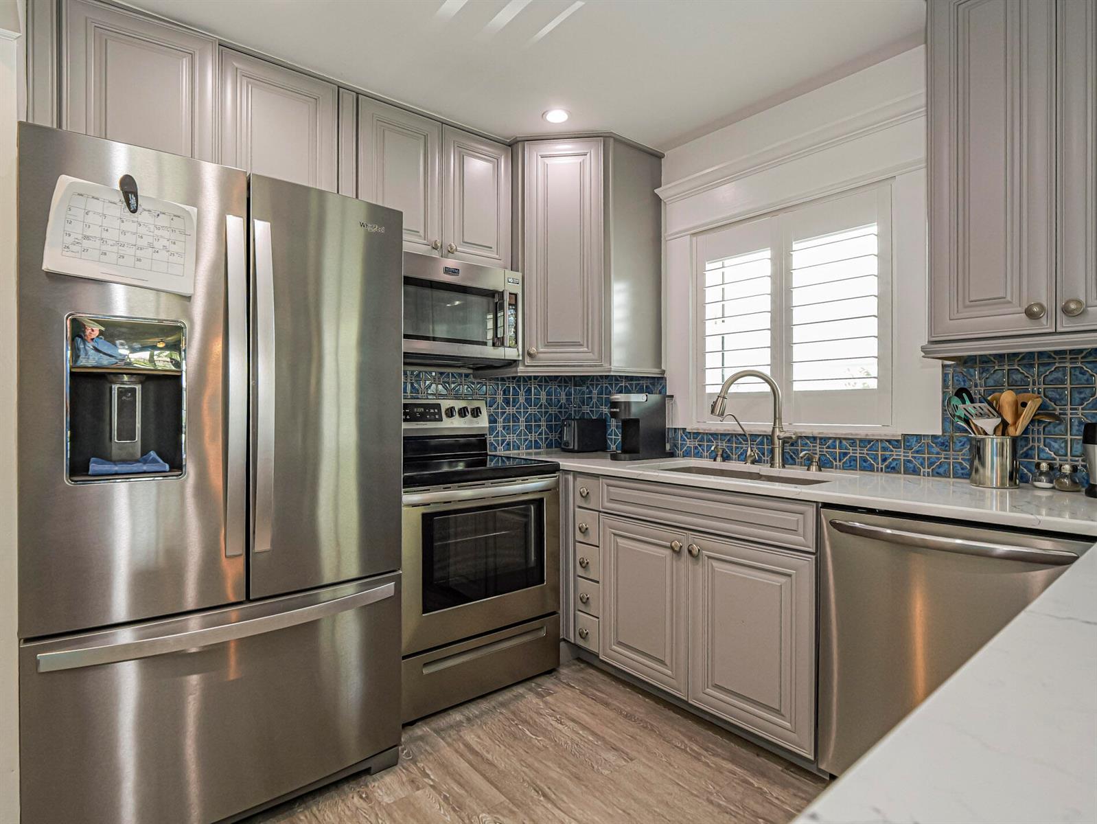 A kitchen features grey cabinets, stainless steel appliances, a blue patterned backsplash, and white countertops — 85 Crooked Tree Lane # 207, Vero Beach FL 32962, VERO BEACH, FL