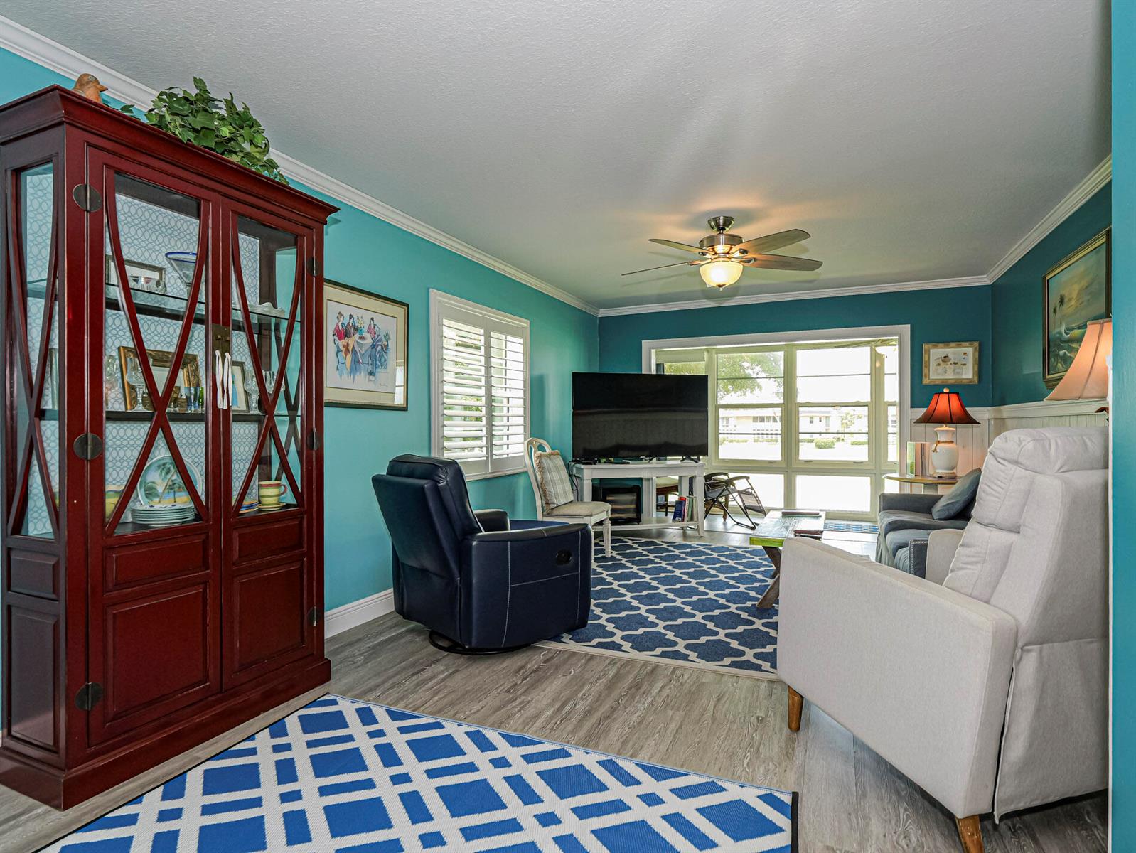 A living room with teal walls, a dark wood cabinet, and a blue patterned rug — 85 Crooked Tree Lane # 207, Vero Beach FL 32962, VERO BEACH, FL