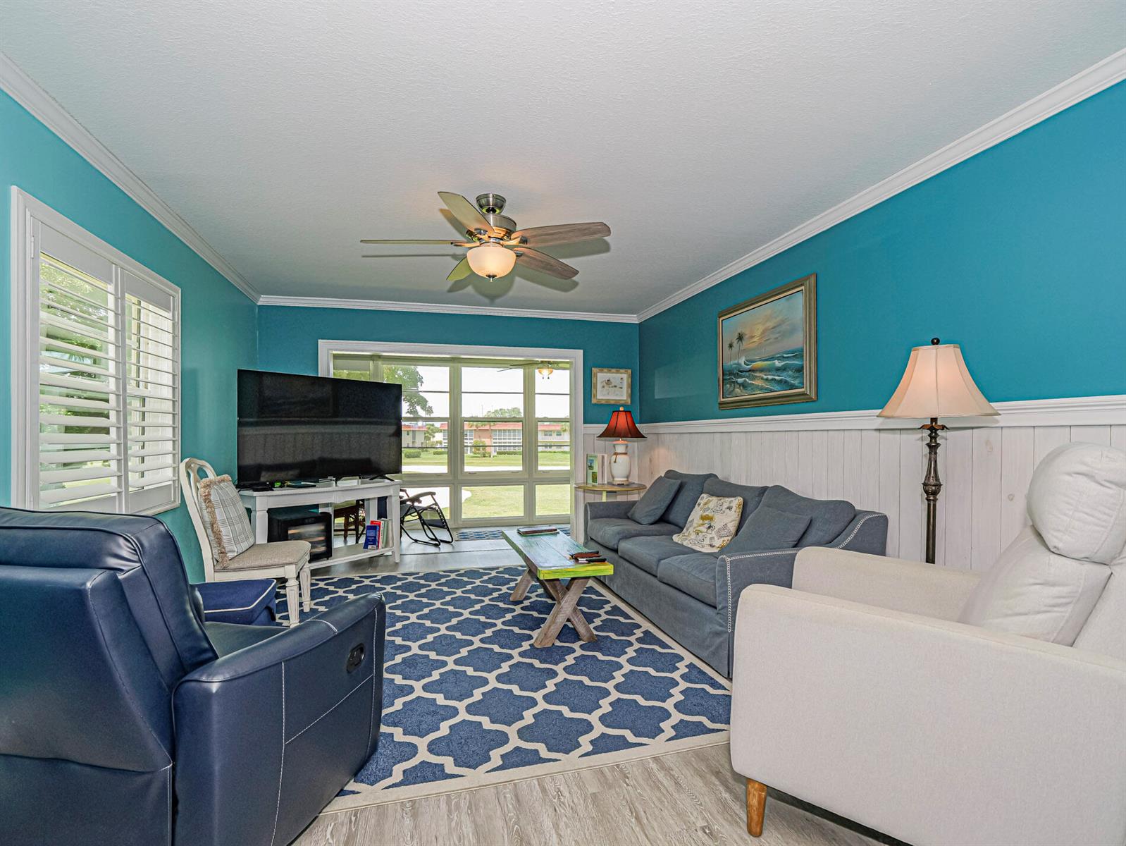A living room features blue walls, white wainscoting, a patterned rug, and a ceiling fan — 85 Crooked Tree Lane # 207, Vero Beach FL 32962, VERO BEACH, FL