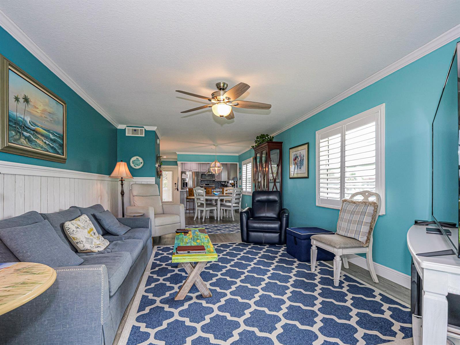 A living room with blue walls, a patterned area rug, and a view into the kitchen — 85 Crooked Tree Lane # 207, Vero Beach FL 32962, VERO BEACH, FL