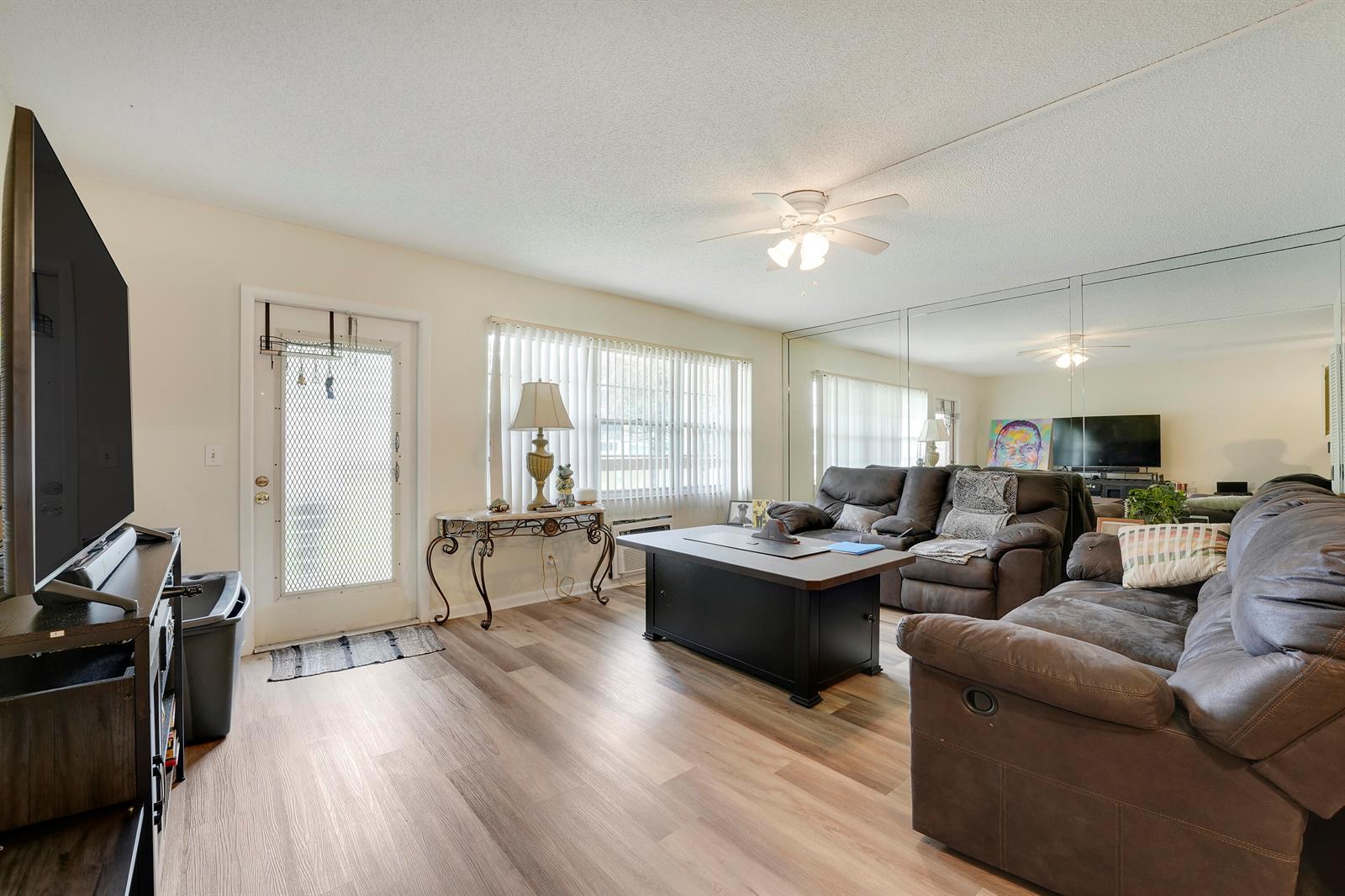 A living room features wood-look flooring, a mirrored wall, a ceiling fan, and brown furniture — 146 Mansfield D, Boca Raton FL 33434, BOCA RATON, FL