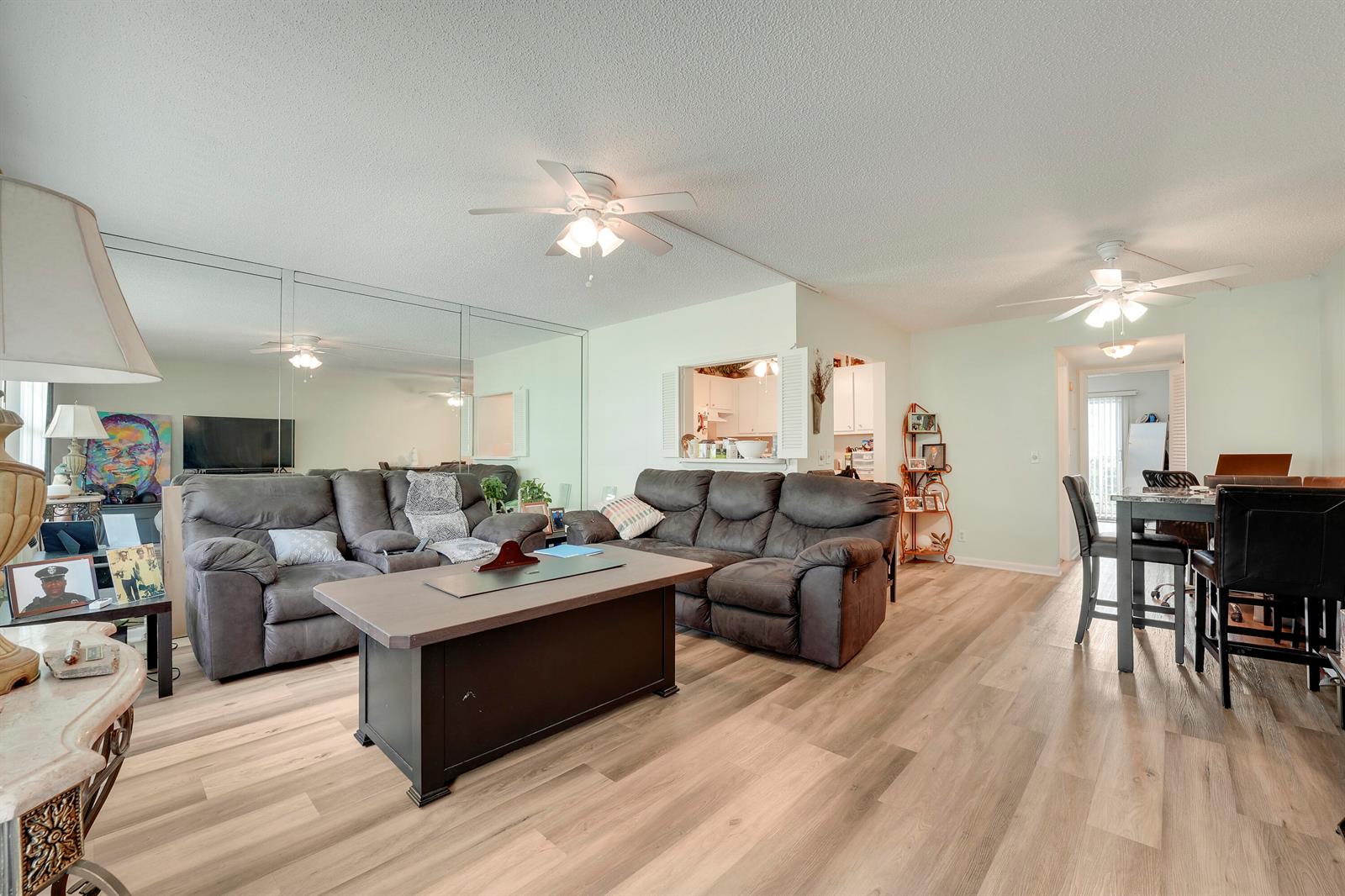 A living room with wood-look flooring, two dark sofas, a coffee table, and mirrored walls — 146 Mansfield D, Boca Raton FL 33434, BOCA RATON, FL
