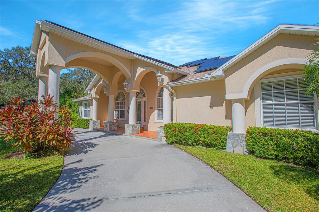 A beige house exterior features a covered arched entryway, a concrete driveway, and solar panels — 4735 CHELSEA COURT, KISSIMMEE, FL