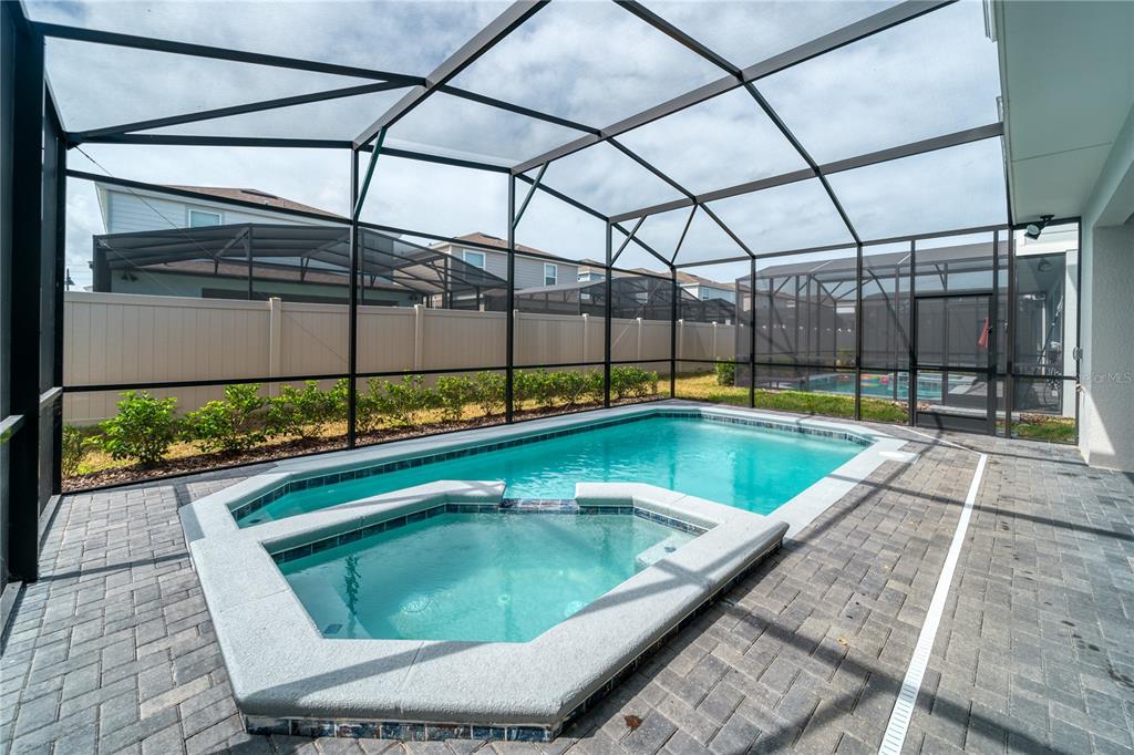 A screened-in patio features a swimming pool and attached spa with paver decking — 3436 LILAC WAY, DAVENPORT, FL