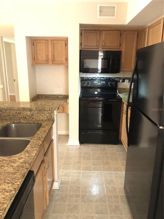 A kitchen features light wood cabinets, granite countertops, black appliances, and light-colored tile flooring — 486 N PIN OAK PLACE UNIT 206, LONGWOOD, FL