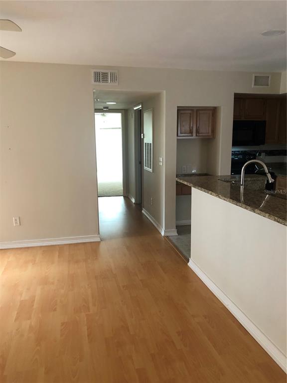 A view of a kitchen with granite countertops and a hallway leading to a doorway — 486 N PIN OAK PLACE UNIT 206, LONGWOOD, FL