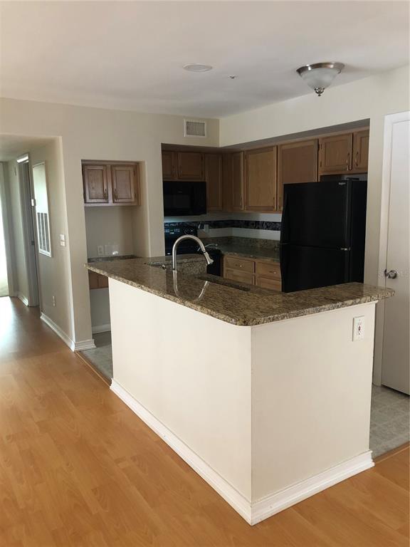 A kitchen with wood cabinets, granite countertops, and a black refrigerator — 486 N PIN OAK PLACE UNIT 206, LONGWOOD, FL