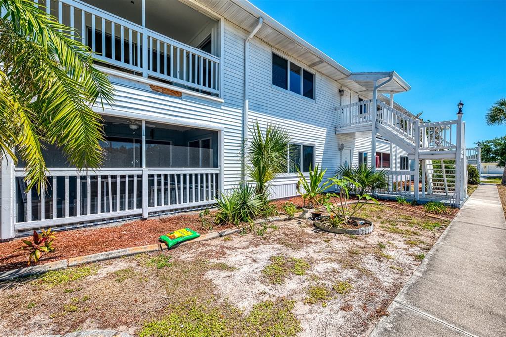 The exterior of a two-story white building features screened porches, a wooden staircase, and landscaping — 200 ROTONDA BOULEVARD W UNIT A2, ROTONDA WEST, FL